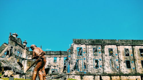 Soldier statue by old ruin historic building against clear blue sky