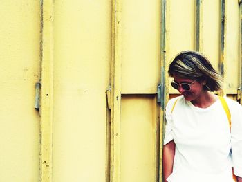 Young woman wearing sunglasses standing against wall