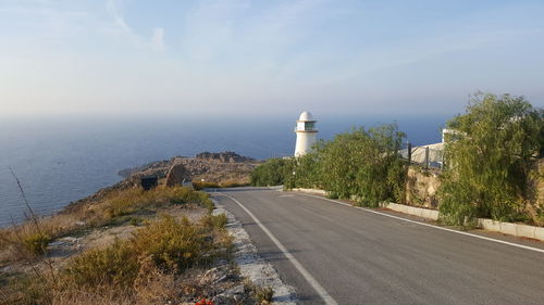 Road by lighthouse by sea against sky