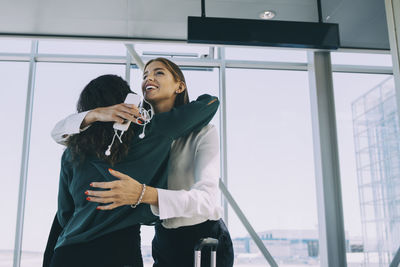 Low angle view of smiling businesswoman embracing colleague in corridor at airport