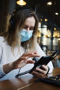 Woman wearing mask using smart phone sitting at cafe