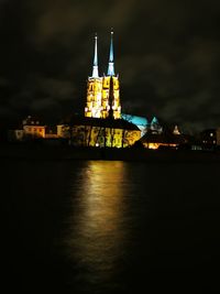 Illuminated building by river against sky at night