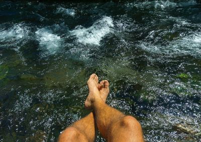 Low section of man dangling legs over lake