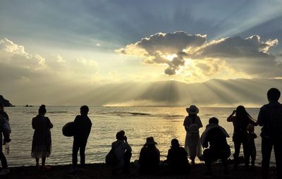 Rear view of people at beach against cloudy sky during sunset