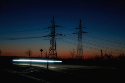 Silhouette electricity pylons on field against sky at sunset