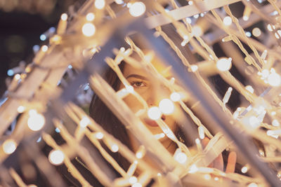Portrait of woman looking through illuminated christmas lights at night
