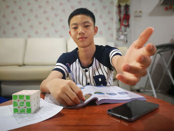 Portrait of boy gesturing while sitting with book on table