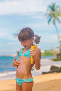 Happy girl applying suntan lotion on stomach at beach