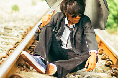 Businessman with umbrella sitting on railroad track