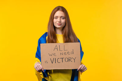 Portrait of young woman holding book against yellow background