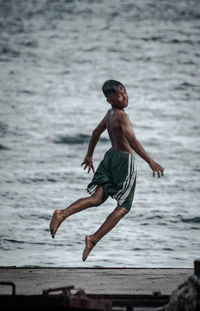 Full length of shirtless man jumping at beach