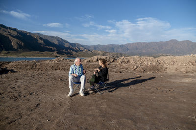 Woman and her grandfather talking while sitting on camping chairs outdoors in nature.