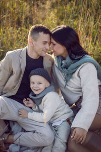 Family of three people mom, dad, son are sitting on the field in autumn