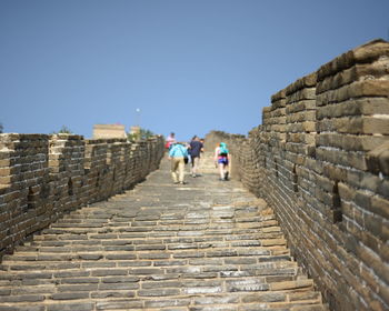 People walking on footpath against clear blue sky