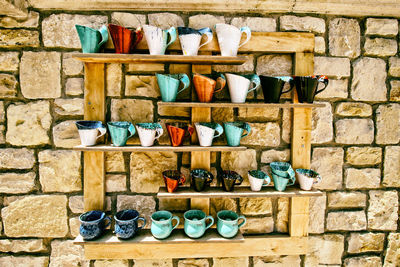 Close-up of cups on shelf against brick wall