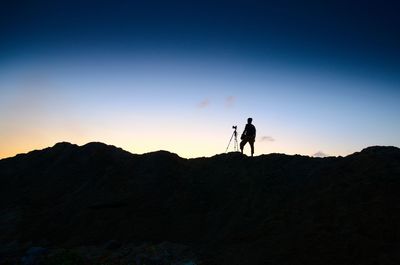 Silhouette man standing on rock against sky during sunset