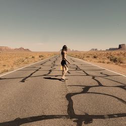 Rear view of woman walking on desert road. 