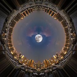Low angle view of buildings against cloudy sky with moon in center