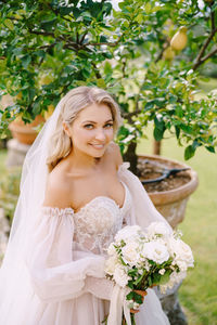 Portrait of smiling bride with bouquet standing outdoors