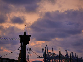 Low angle view of silhouette cranes against buildings during sunset