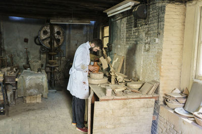 Craftsman examining ceramic pot standing at workbench in factory