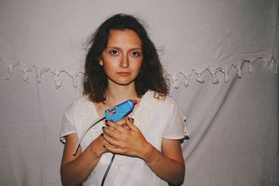 Portrait of woman holding glue gun against white curtain