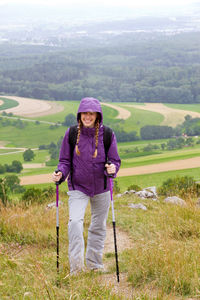 Portrait of female hiker standing on field against sky