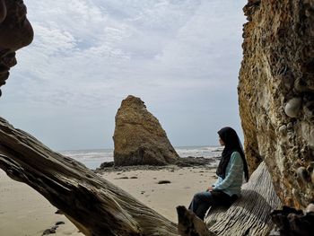 Woman sitting on rock by sea against sky