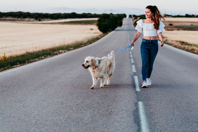 Woman walking with dog on road amidst field