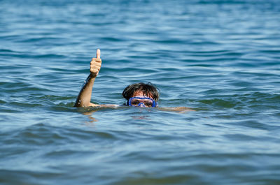 Woman wearing scuba mask in sea showing thumbs up