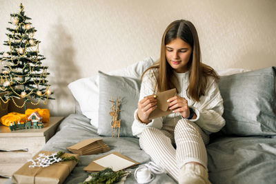 Smiling girl holding envelope sitting on bed at home