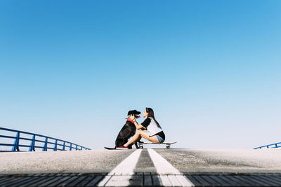 People sitting on railing against clear blue sky