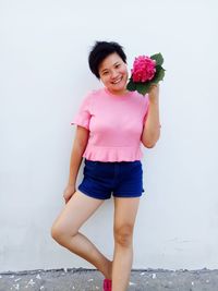 Portrait of happy mid adult woman holding pink flower by wall