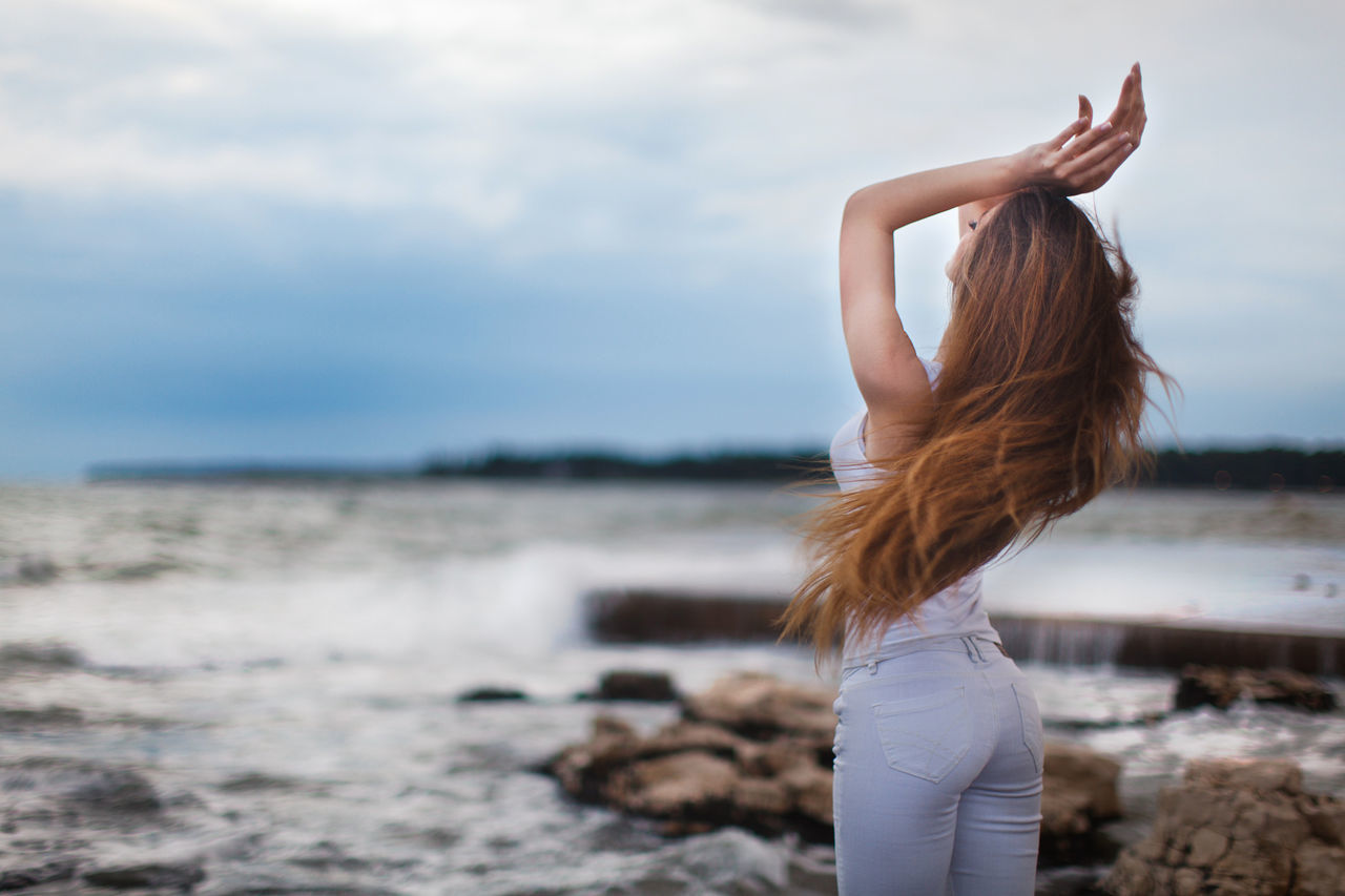 water, sea, young adult, one person, nature, sky, arms raised, gesturing, leisure activity, real people, lifestyles, young women, women, outdoors, beach, standing, beauty in nature, day, horizon over water, one young woman only, people