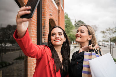 Portrait of smiling young woman using mobile phone in city