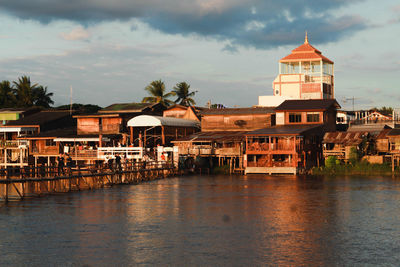 Buildings at waterfront against cloudy sky