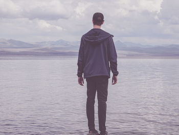 Rear view of man standing on sea against sky