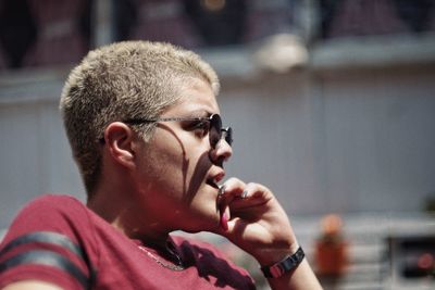 Close-up of young woman wearing sunglasses looking away while sitting outdoors