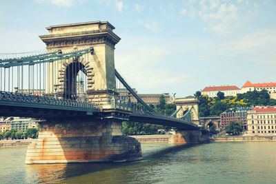 Bridge over river in city against cloudy sky