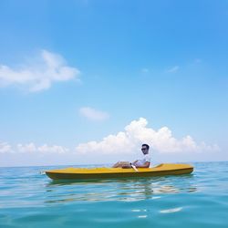 Side view of man sitting on rowboat in sea against sky