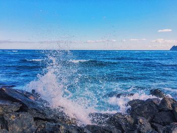 Wave splashing on rock at sea shore against sky