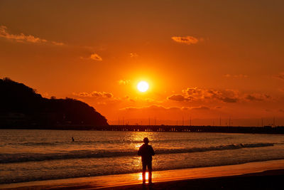 Silhouette people standing on beach against sky during sunset