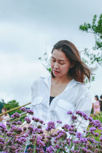 Beautiful woman standing by flowering plants against sky