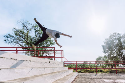 Back view of anonymous male jumping above staircase in city and performing parkour stunt