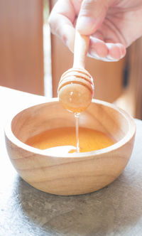 Cropped hand of person holding honey dipper over bowl on table