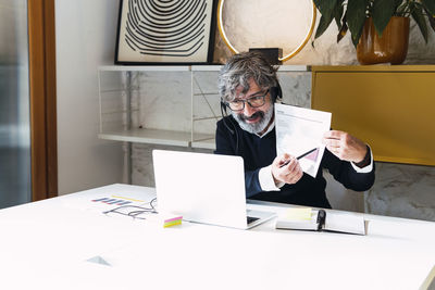 Senior freelancer wearing headset explaining document sitting at table