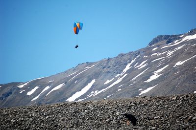 Person paragliding over mountain against sky