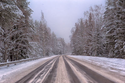 Road amidst snow covered trees against sky