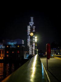 Illuminated buildings by river against sky at night