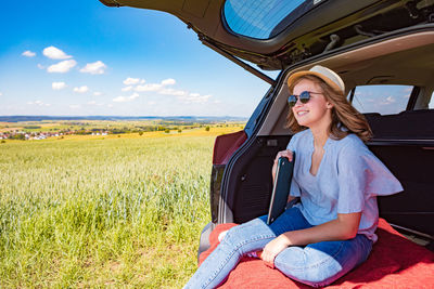 Woman sitting on field against sky